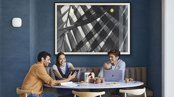 Group of young adults in a cafe on their devices with an eero PoE 6 on the wall